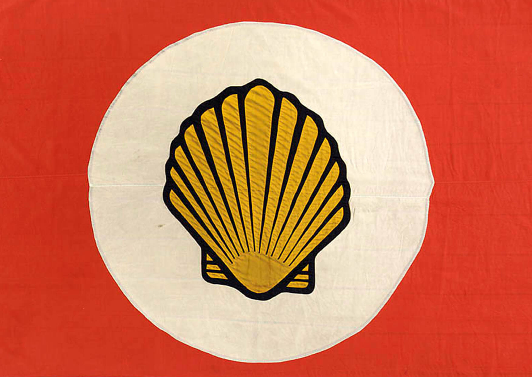 Color photo of a flag showing the Shell Logo in white circle on a red background